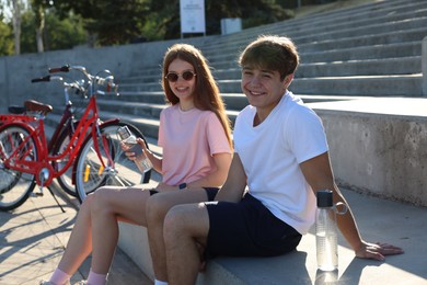Photo of Teenage girl and boy sitting on stairs near bicycles on city street