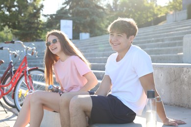 Photo of Teenage girl and boy sitting on stairs near bicycles on city street