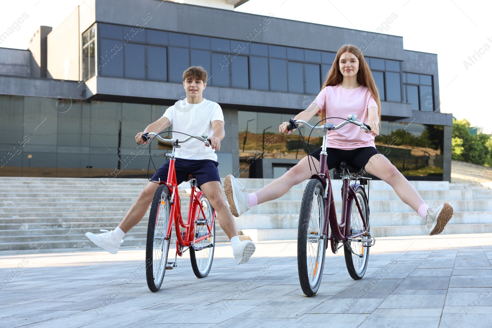 Teenage girl and boy riding bicycles on city street Photo of Teenage girl and boy riding bicycles on city street