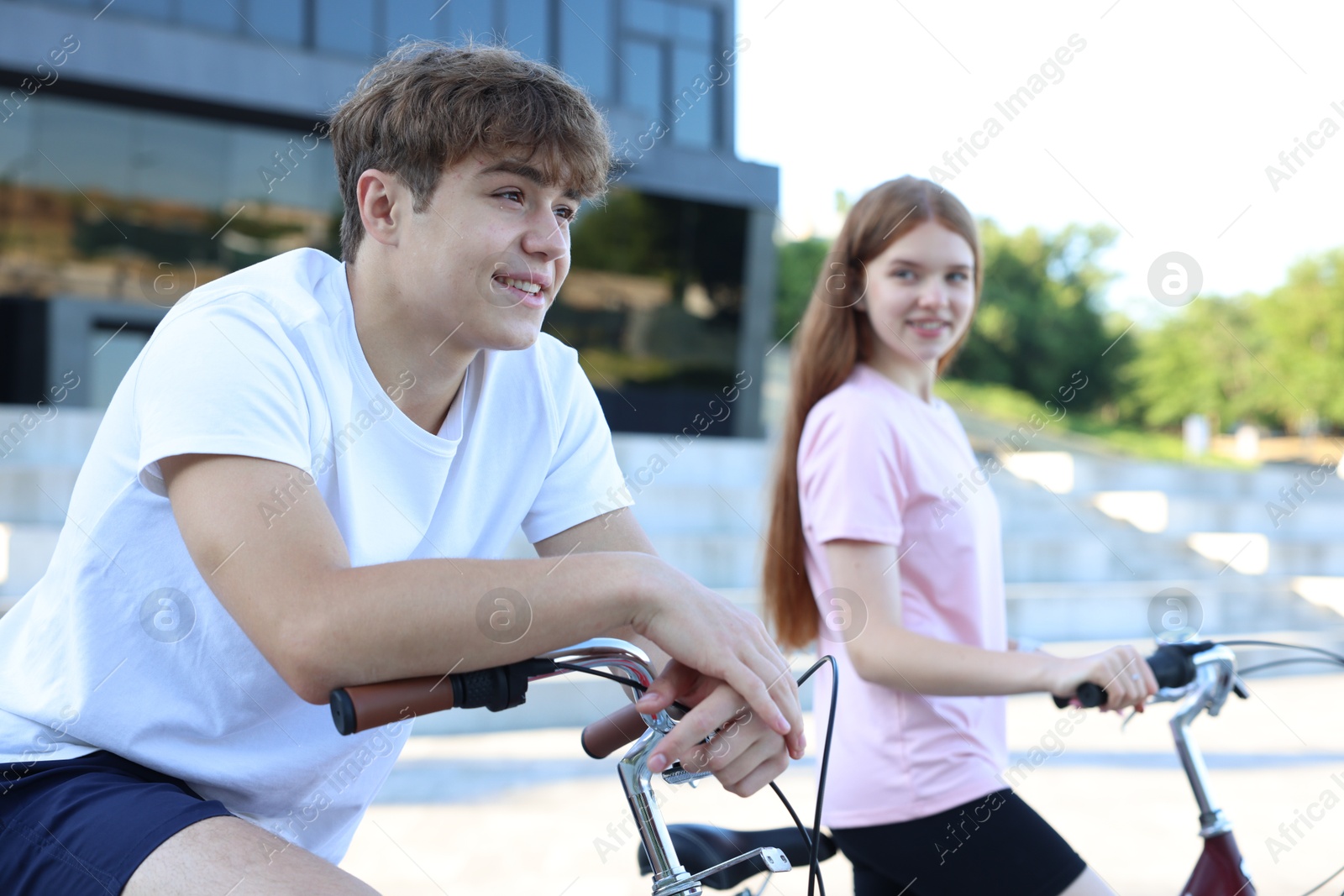 Photo of Teenage girl and boy riding bicycles on city street, selective focus