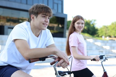Photo of Teenage girl and boy riding bicycles on city street, selective focus