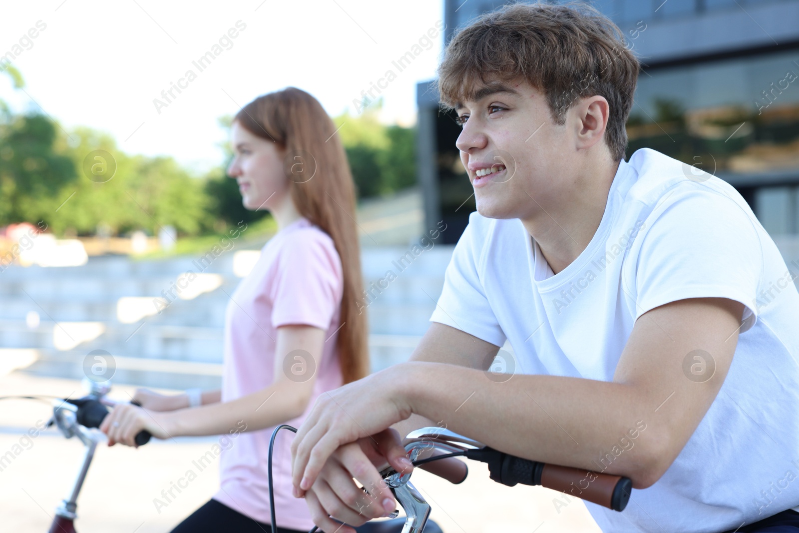 Photo of Teenage girl and boy riding bicycles on city street, selective focus
