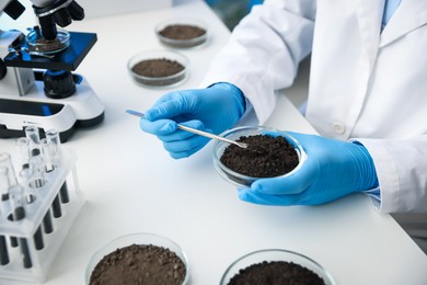 Photo of Scientist taking soil sample for research at white table in laboratory, closeup