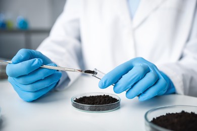 Photo of Scientist taking soil sample for research at white table in laboratory, closeup