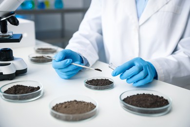 Photo of Scientist taking soil sample for research at white table in laboratory, closeup