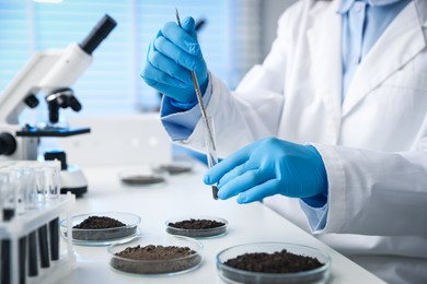 Photo of Scientist taking soil sample for research at white table in laboratory, closeup
