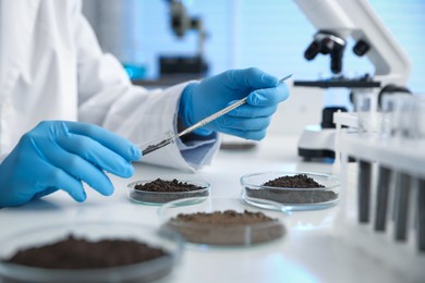 Photo of Scientist taking soil sample for research at white table in laboratory, closeup