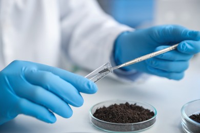 Photo of Scientist taking soil sample for research at white table in laboratory, closeup