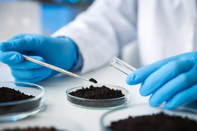 Photo of Scientist taking soil sample for research at white table in laboratory, closeup
