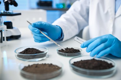 Photo of Scientist taking soil sample for research at white table in laboratory, closeup