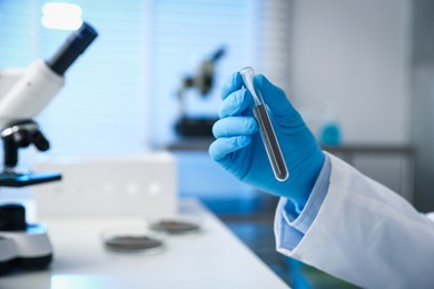 Photo of Scientist with test tube of soil sample at white table in laboratory, closeup