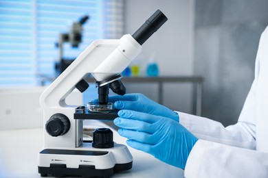 Photo of Scientist researching soil sample with microscope at white table in laboratory, closeup