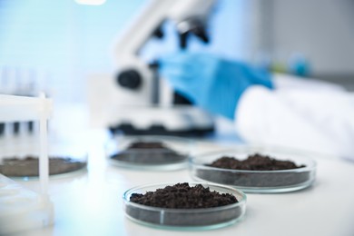 Photo of Scientist working at white table in laboratory, focus on Petri dishes with soil samples