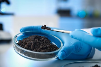 Photo of Scientist taking soil sample for research at white table in laboratory, closeup