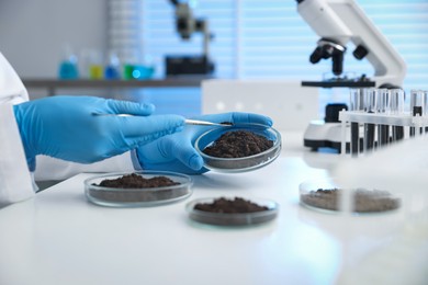 Photo of Scientist taking soil sample for research at white table in laboratory, closeup
