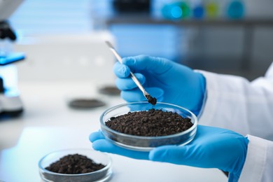 Photo of Scientist taking soil sample for research at white table in laboratory, closeup