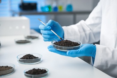 Photo of Scientist taking soil sample for research at white table in laboratory, closeup