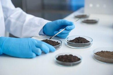 Photo of Scientist taking soil sample for research at white table in laboratory, closeup