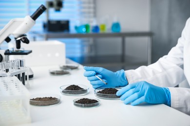 Photo of Scientist taking soil sample for research at white table in laboratory, closeup