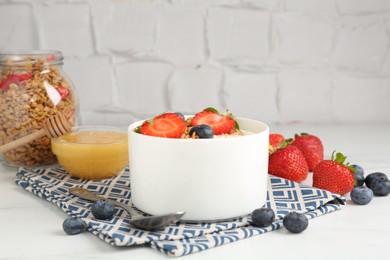 Photo of Tasty yogurt with granola, berries and honey on white table, closeup