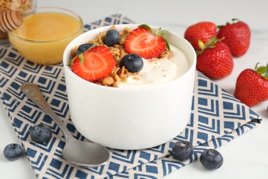 Photo of Tasty yogurt with granola, berries and honey on white table, closeup
