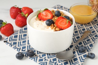 Photo of Tasty yogurt with granola, berries and honey on white table, closeup