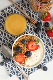 Photo of Tasty yogurt with granola, berries and honey on white table, flat lay
