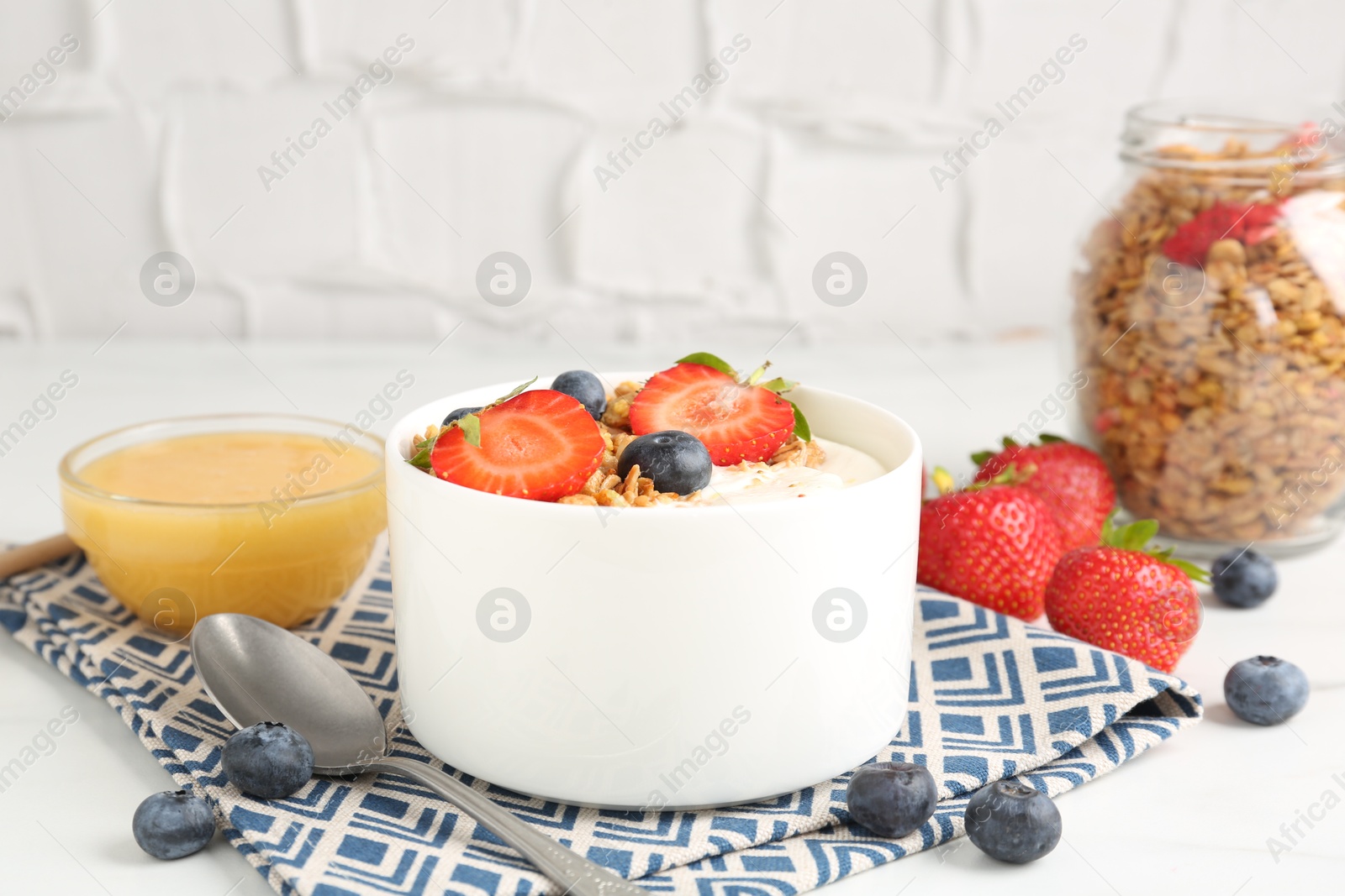 Photo of Tasty yogurt with granola, berries and honey on white table, closeup