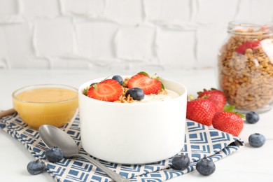 Photo of Tasty yogurt with granola, berries and honey on white table, closeup