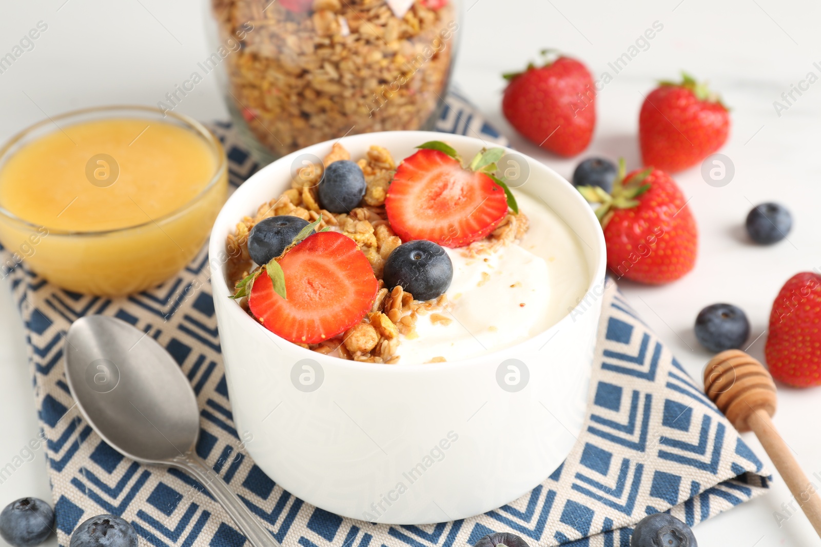 Photo of Tasty yogurt with granola, berries and honey on table, closeup