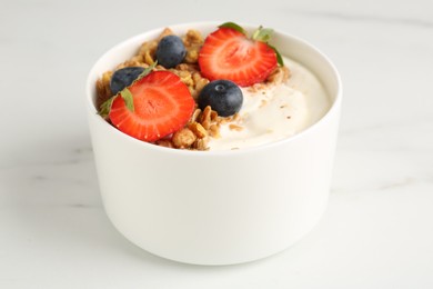 Photo of Tasty yogurt with granola and berries on white marble table, closeup