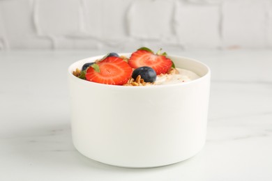 Photo of Tasty yogurt with granola and berries on white marble table, closeup