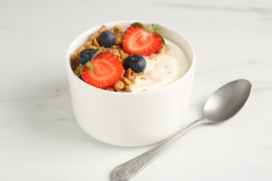 Photo of Tasty yogurt with granola, berries and spoon on white marble table, closeup
