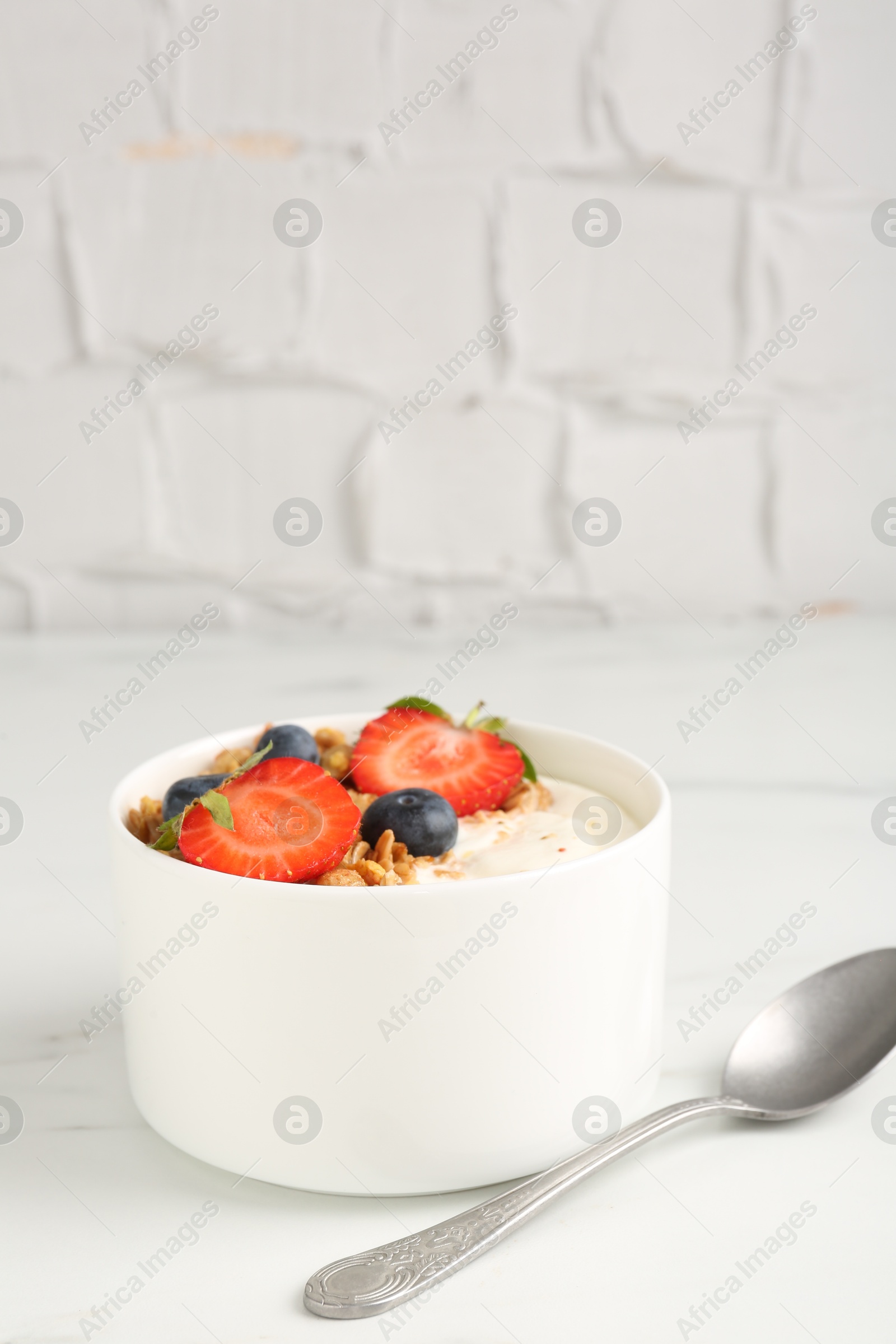 Photo of Tasty yogurt with granola, berries and spoon on white marble table, closeup