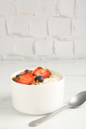 Photo of Tasty yogurt with granola, berries and spoon on white marble table, closeup
