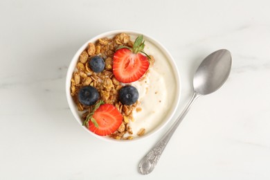 Photo of Tasty yogurt with granola, berries and spoon on white marble table, flat lay