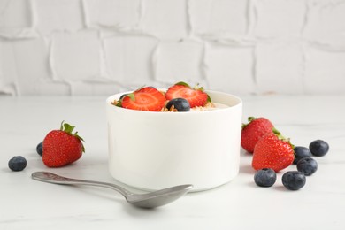 Photo of Tasty yogurt with granola, berries and spoon on white marble table, closeup