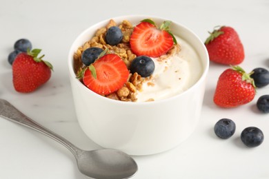Photo of Tasty yogurt with granola, berries and spoon on white marble table, closeup