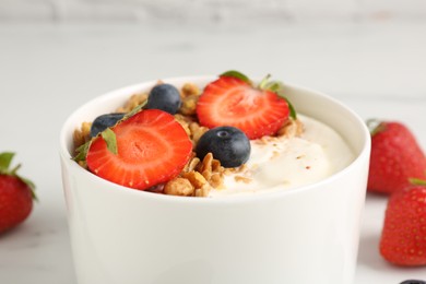Photo of Tasty yogurt with granola and berries on white table, closeup