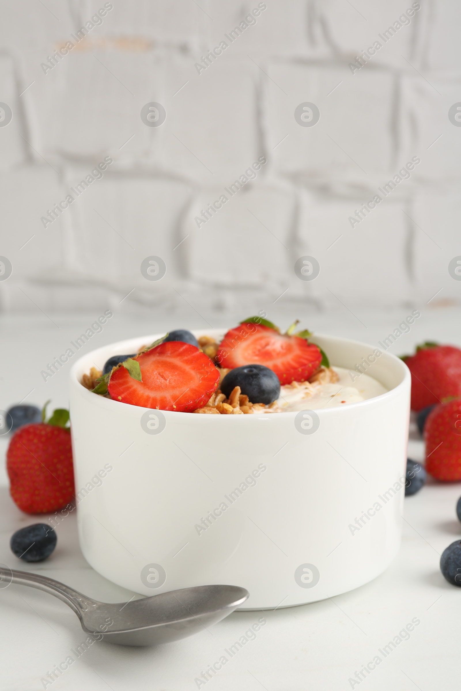 Photo of Tasty yogurt with granola, berries and spoon on white table, closeup