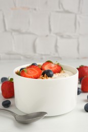 Photo of Tasty yogurt with granola, berries and spoon on white table, closeup