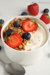 Photo of Tasty yogurt with granola, berries and spoon on white table, closeup
