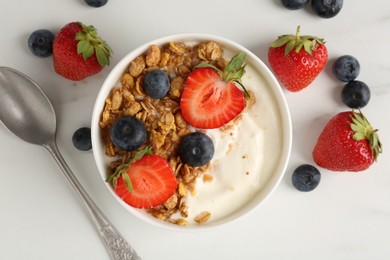 Photo of Tasty yogurt with granola, berries and spoon on white marble table, flat lay
