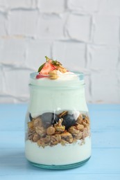 Photo of Tasty yogurt with granola and berries in glass jar on light blue wooden table, closeup