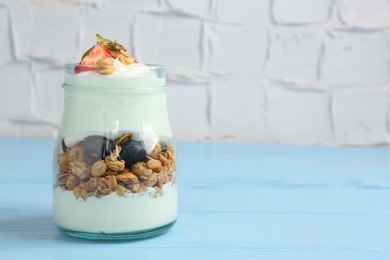 Photo of Tasty yogurt with granola and berries in jar on light blue wooden table, closeup. Space for text