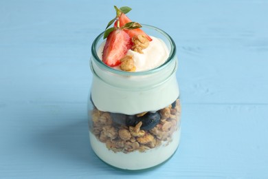 Photo of Tasty yogurt with granola and berries in glass jar on light blue wooden table, closeup