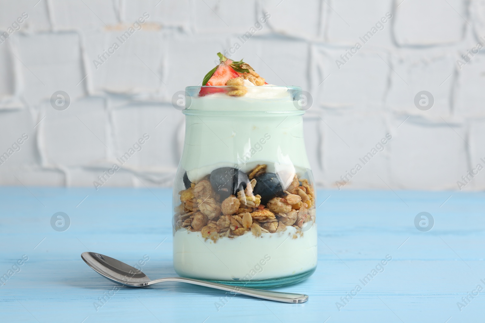 Photo of Tasty yogurt with granola and berries in glass jar on light blue wooden table