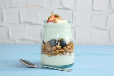 Photo of Tasty yogurt with granola and berries in glass jar on light blue wooden table