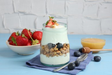 Photo of Tasty yogurt with granola, berries, honey and spoon on light blue wooden table