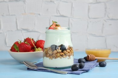 Photo of Tasty yogurt with granola, berries, honey and spoon on light blue wooden table
